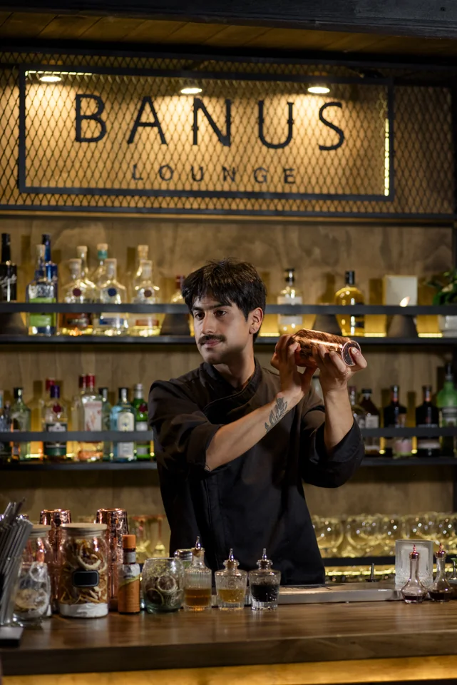 Bartender agitando una coctelera de cobre frente al letrero de Banús Lounge.